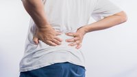 Orthopädiezentrum Wien - Ein Mann hält sich mit beiden Händen den Rücken aufgrund von Schmerzen durch Facettenarthrosen.