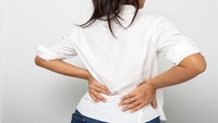 Orthopädiezentrum Wien - Ein Mann stützt sich mit den Händen am unteren Rücken und zeigt Beschwerden, die auf Spondylarthrose hindeuten.